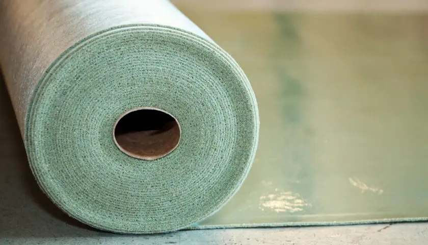 Rotolo di materiale per insonorizzare pavimento, con texture fibrosa e colore verde chiaro.