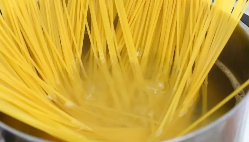 Długie, żółte nitki makaronu spaghetti gotują się w bulgoczącej wodzie. Kluczowe jest, ile posolić makaron, by był idealny.