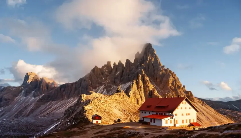 Sonnenuntergang an einer Berghütte. Die schroffen Gipfel der Dolomiten ragen hinter dem Gebäude auf. Hier könnte man gut zwei Wochen auf der Alm arbeiten.
