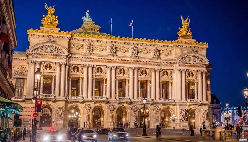 Słynny teatr w Paryżu, Opera Garnier, lśni w nocnym świetle. Złote rzeźby i bogata fasada zapraszają na wieczór pełen wrażeń.