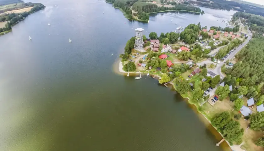 Widok z lotu ptaka na zalew zemborzycki z żaglówkami, domkami i wieżą widokową.