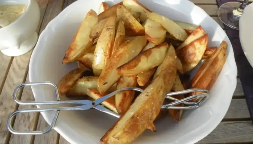 En skål med gyllene klyftpotatis i ugn, redo att serveras med en sallad och dipp.