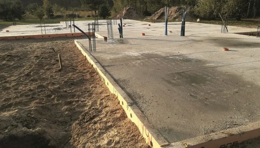 Szalunek płyty fundamentowej z widocznymi zbrojeniami i instalacjami. Betonowa płyta fundamentowa w trakcie budowy.