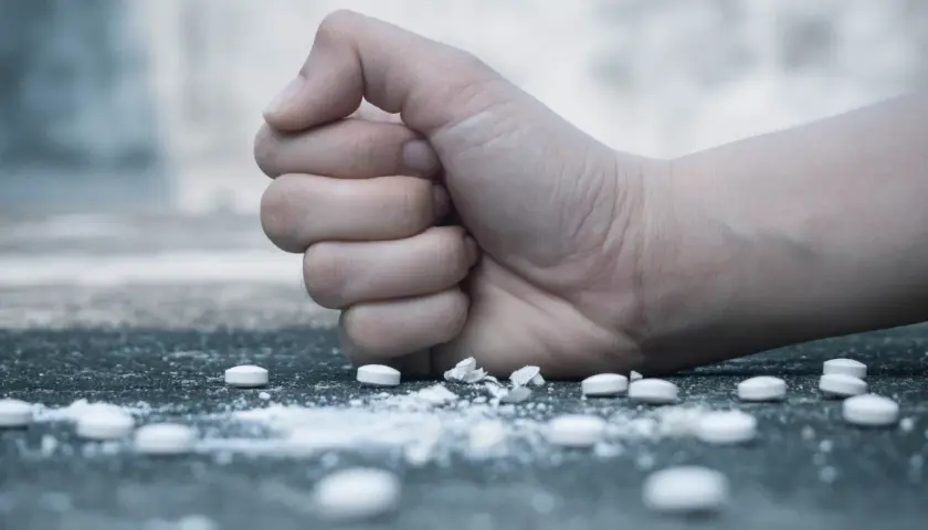 Zaciśnięta pięść nad białym proszkiem i tabletkami, symbolizująca walkę z nałogiem, np. flakka.