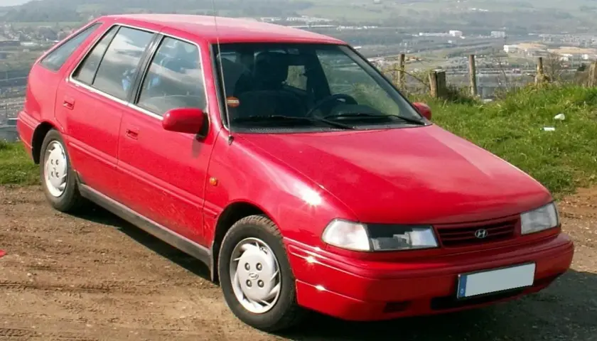 Czerwony Hyundai Pony stoi na polnej drodze, z widokiem na krajobraz w tle.