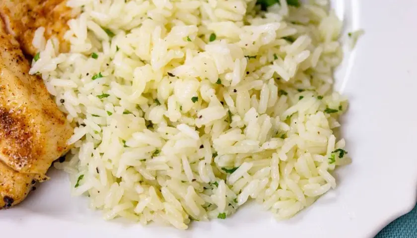 Fluffy white rice with flecks of green herbs, perfect for a simple rice seasoning recipe. A side of grilled chicken is visible.