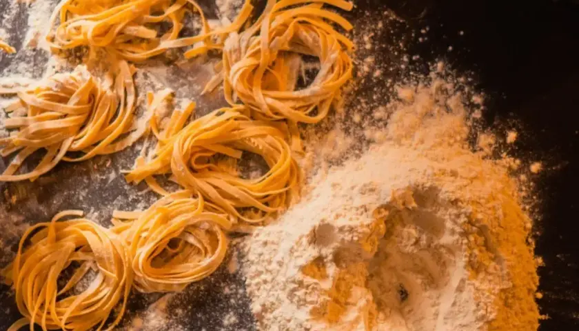 Domowy makaron, jak u babci! Świeże tagliatelle uformowane w gniazda, obok kopczyka mąki. Przepis babci na pyszne danie.