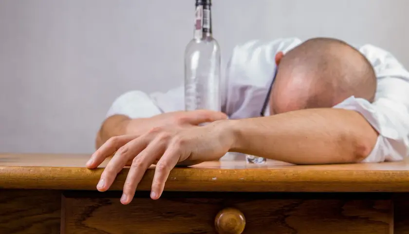 Mężczyzna śpi na biurku obok pustej butelki. Czy alkohol wypłukuje żelazo? To pytanie zadaje sobie wielu.