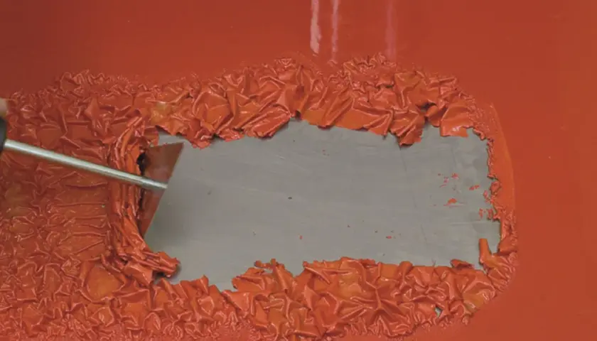 Mit einem Spachtel werden orangefarbene Lackflecken entfernt.
