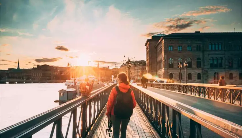 En person med ryggsäck promenerar i Stockholm vid solnedgången över vattnet.