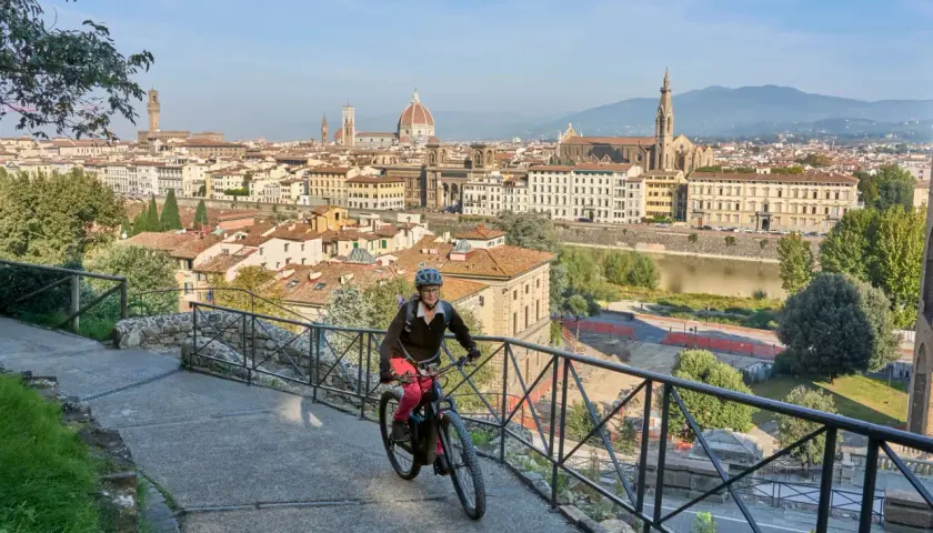 A woman enjoys an Italy bike tour, cycling with Florence's iconic skyline behind her.