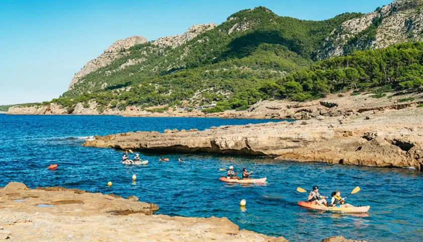 Kajakfahrer erkunden eine felsige Bucht mit türkisfarbenem Wasser und bewaldeten Bergen im Hintergrund. Perfekt für die Frage: wohin auf Mallorca?