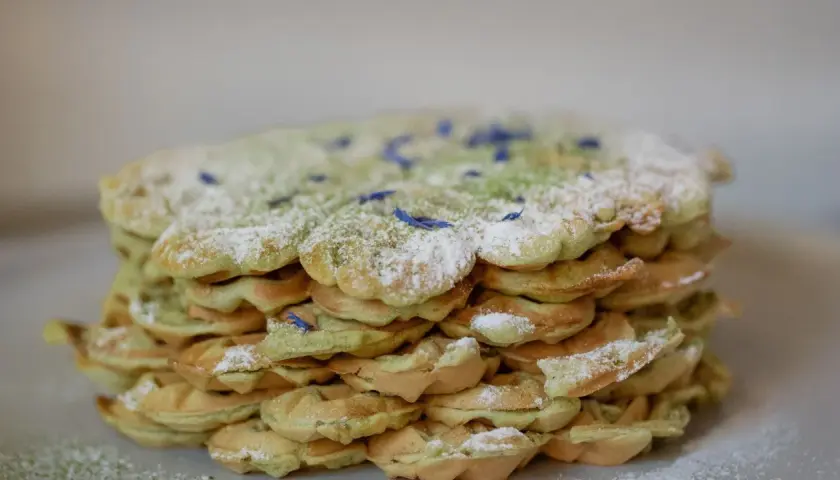 Ein Stapel leckerer Matcha Waffeln, bestäubt mit Puderzucker und verziert mit blauen Blütenblättern.