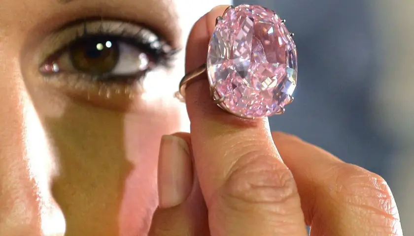 Ein riesiger, pinker Diamantring wird von einer Hand gehalten. Man fragt sich, wie viel kostet ein Kilo Diamant?