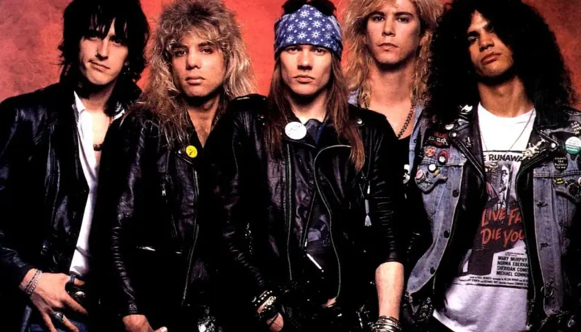 Guns N' Roses członkowie w skórzanych kurtkach i z charakterystycznymi fryzurami. Axl Rose w bandanie, Slash z burzą loków.