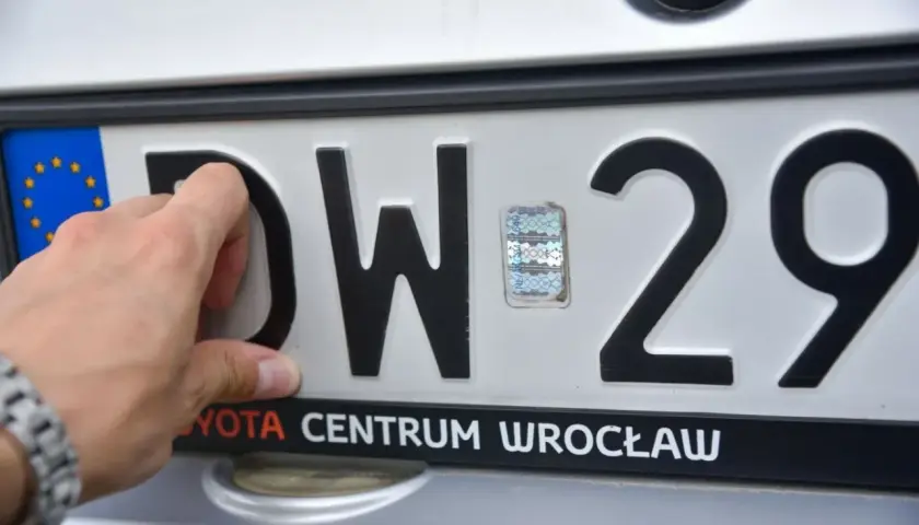 Dłoń przykłada tablicę rejestracyjną na bagażnik rowerowy. Widoczne litery DW i cyfry 29.