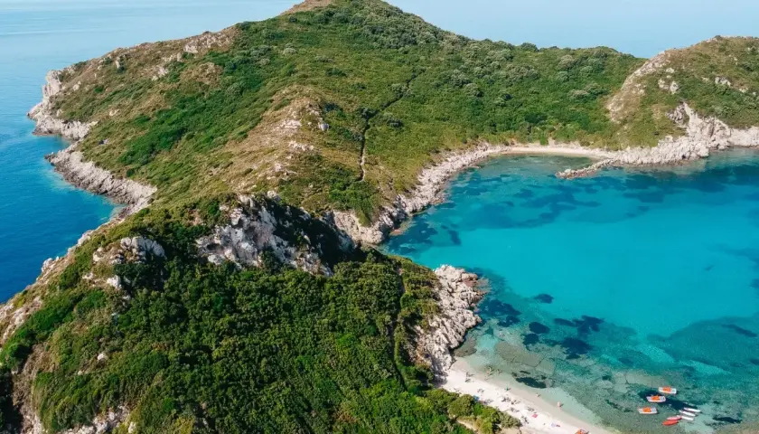 Idealna pogoda na Korfu we wrześniu: turkusowa zatoka, zielone wzgórza i piaszczysta plaża z łódkami.