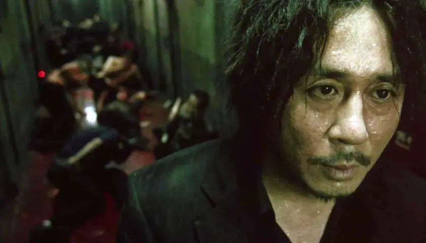 Primo piano di un uomo sudato, con un'espressione intensa, sullo sfondo una scena confusa di persone. Ricorda il film Oldboy e il suo polpo.