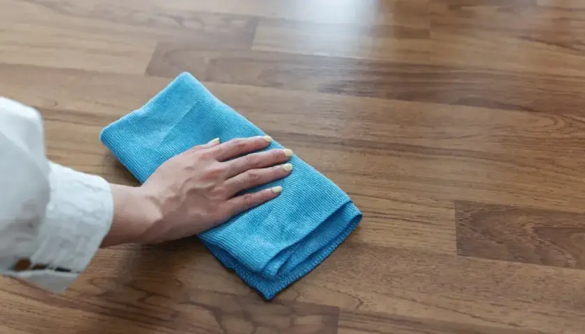 Mano con panno blu pulisce pavimento in gres effetto legno. Scopri come togliere la colla dal pavimento in gres con metodi efficaci.