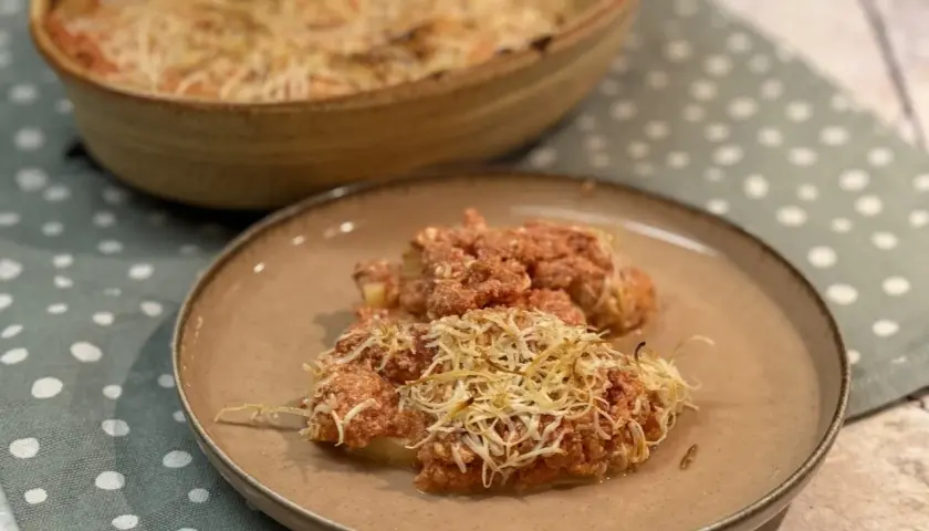 Dos porciones de gnocchi alla romana gratinados con queso, servidos en un plato marrón sobre un mantel de lunares.