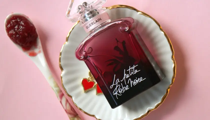 Elegancka buteleczka perfum Guerlain La petite robe noire z uroczymi serduszkami, obok łyżeczka z dżemem.