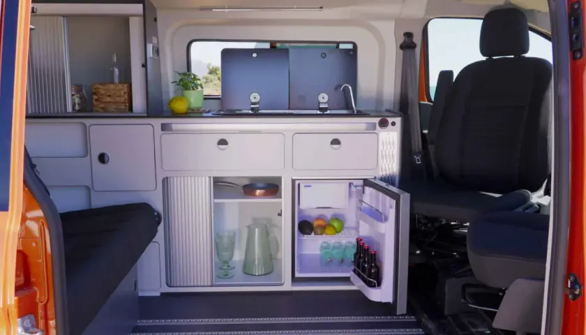 Aménagement astucieux de la soute d'un camping-car : cuisine fonctionnelle, réfrigérateur et rangements optimisés pour un voyage serein.
