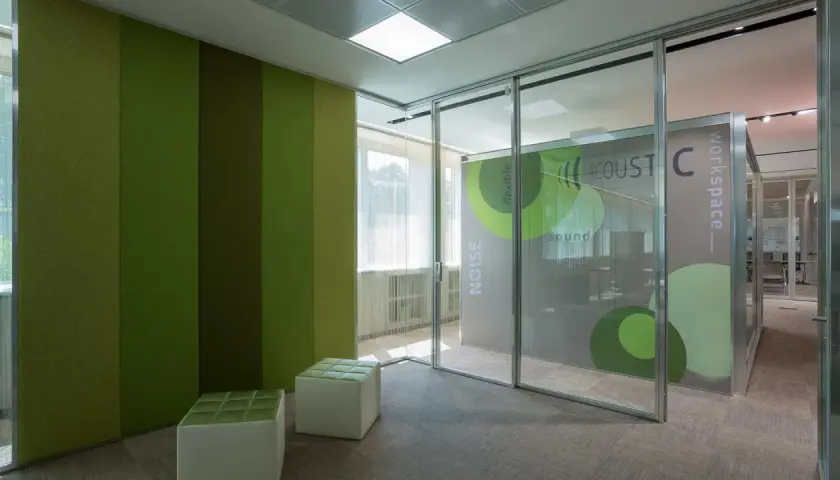 Pannelli verdi a parete e divisori fonoassorbenti creano un ambiente di lavoro moderno e silenzioso.