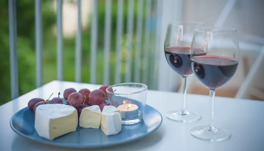 Dwa kieliszki czerwonego wina, talerz z serem camembert, winogronami i świecą.
