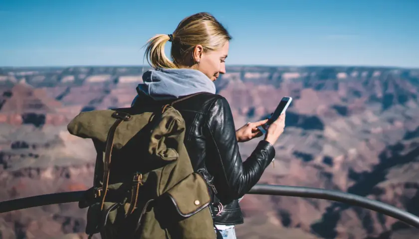 Kobieta z plecakiem w Wielkim Kanionie sprawdza telefon, planując dalszą podróż – roaming krajowy a międzynarodowy.