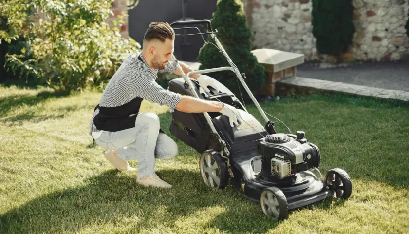 Mężczyzna w fartuchu sprawdza kosiarkę, zastanawiając się, na jaką wysokość kosić trawę, by ogród wyglądał idealnie.