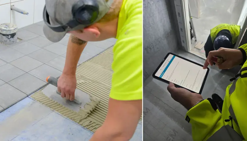Byggare lägger klinker på ett badrumsgolv. En annan person kontrollerar arbetet på en surfplatta.