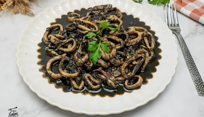 Plato de calamares en su tinta, con anillas tiernas y sabrosas, decorado con perejil fresco. Un clásico irresistible.