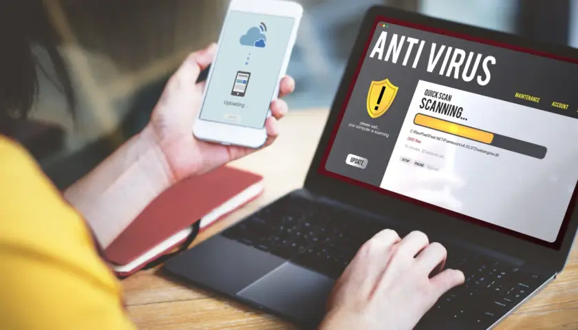 Osoba korzysta z laptopa z programem antywirus free, który skanuje komputer. Na telefonie widnieje komunikat o przesyłaniu danych.