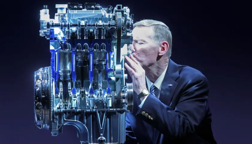 Mężczyzna w garniturze całuje silnik Forda. Wiele osób szuka **1.0 ecoboost opinie** przed zakupem.