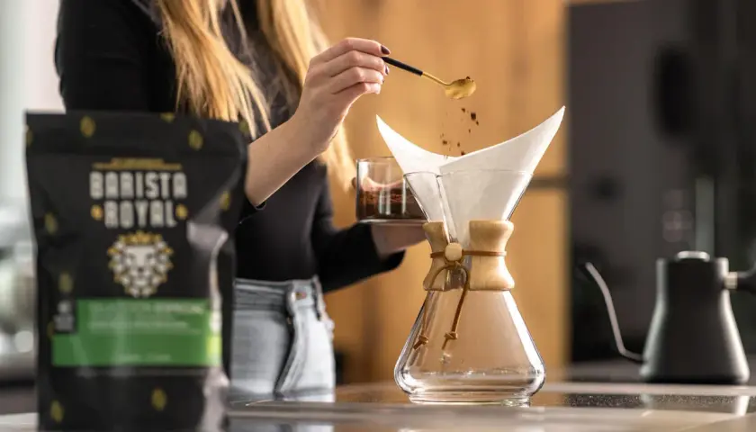 Eine Frau gibt mit einem Löffel Kaffeepulver in einen Chemex-Filter. Die richtige **Filterkaffee Menge** ist entscheidend für den perfekten Geschmack.