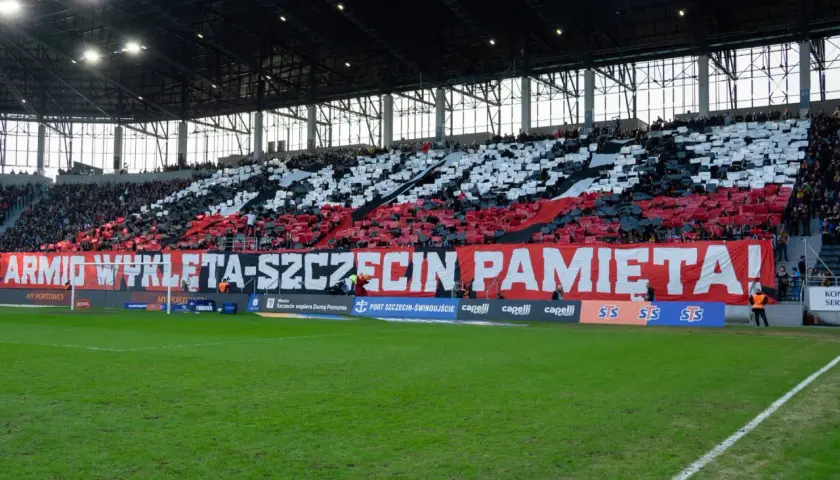 Trybuna stadionu podczas meczu Pogoń Szczecin – Widzew Łódź. Kibice tworzą biało-czerwony transparent "ARMIO WYKLETA-SZCZECIN PAMIĘTA!".