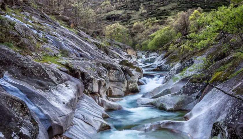 El **camino del agua** serpentea entre rocas erosionadas y vegetación verde, creando un paisaje natural sereno.
