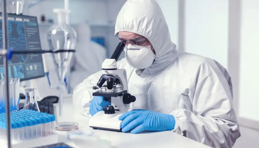Analityk medyczny w kombinezonie ochronnym bada próbki pod mikroskopem w laboratorium.