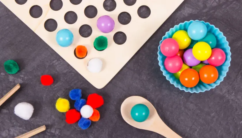 Juego heuristico materiales: pompones, bolas de colores y cuchara de madera para explorar texturas y formas.