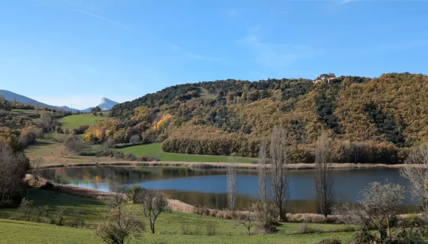 El estany de Montcortès, un espejo de agua sereno rodeado de colinas otoñales y un cielo azul claro.