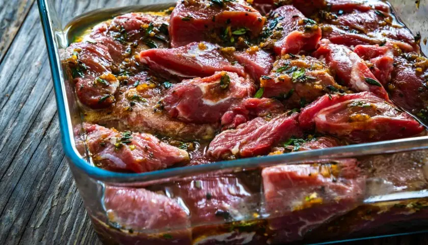 Morceaux de joue de porc marinés dans un plat en verre, prêts à être cuisinés.