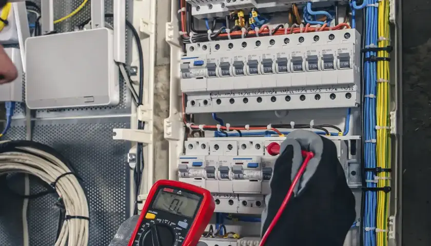 Ein Elektriker prüft mit einem Multimeter eine Schalttafel. Das Bild zeigt die sorgfältige Arbeit, die für ein gutes industrieelektriker gehalt wichtig ist.
