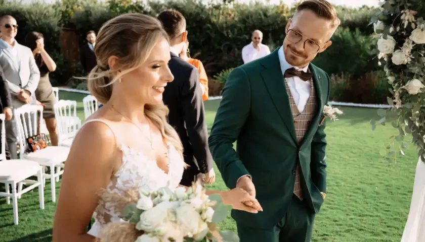 Młoda para trzyma się za ręce podczas ceremonii ślubnej. Ona w białej sukni z bukietem, on w zielonym garniturze. To piękny urlop okolicznościowy ślub.
