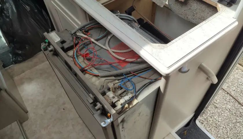 Réparation du frigo camping-car 12v 220v gaz Dometic en panne. Câblage apparent et composants exposés.