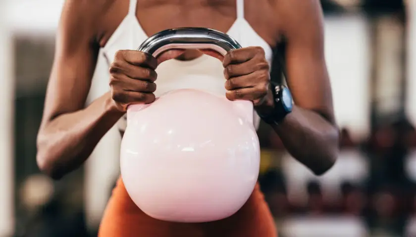 Kobieta z rozbudowanymi ramionami trzyma różową kettlebell, ćwicząc, by badz sprawny jak lampart.