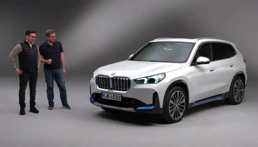 Dwóch mężczyzn obok białego BMW X1 elektryk.