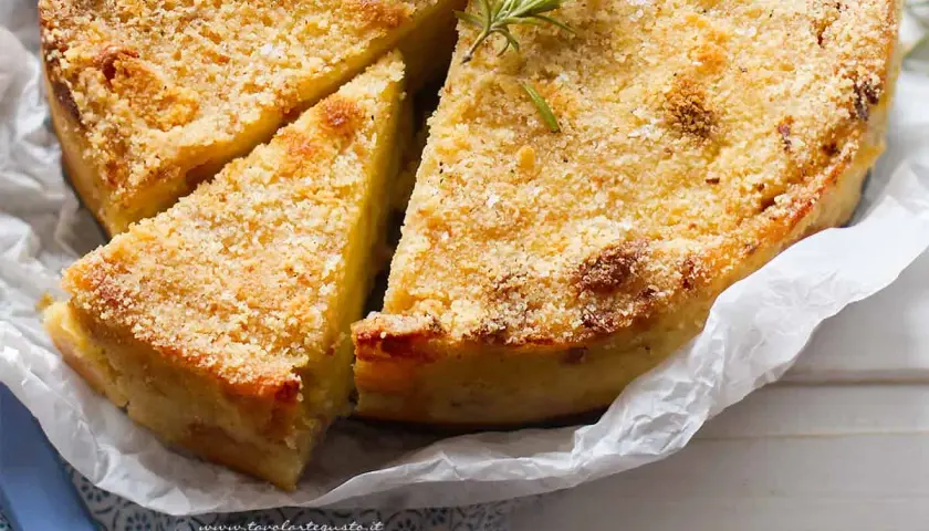 Delizioso gateau di patate dorato e croccante, guarnito con rosmarino fresco. Una fetta è già stata tagliata, invitando ad assaporare questo piatto.