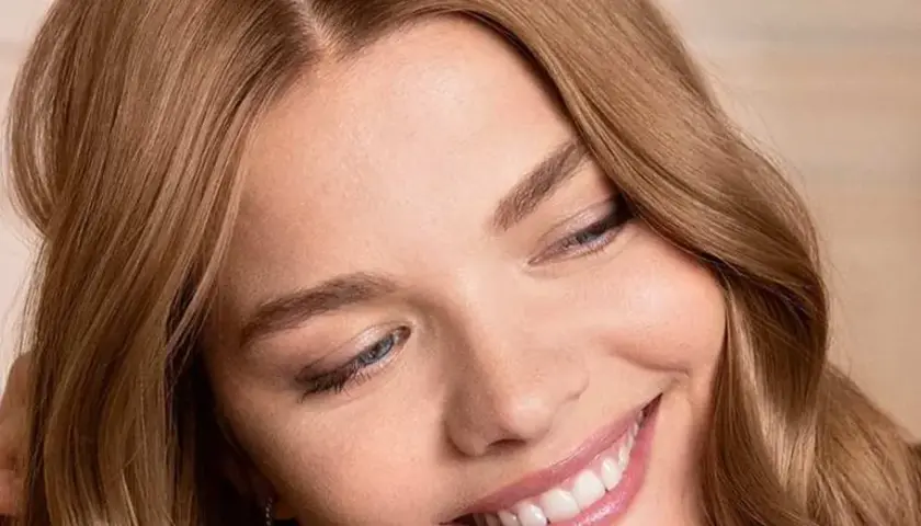 Sonrisa radiante de una mujer con marron ceniza pelo, ojos azules y piel luminosa.