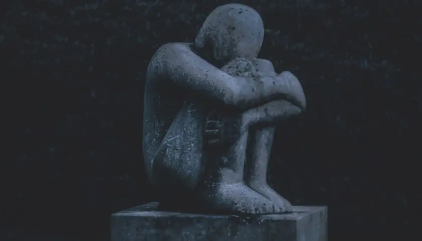 Eine traurige Steinstatue, die sich in sich zusammenkauert, symbolisiert das schlechte Gewissen nach dem Tod des Partners.
