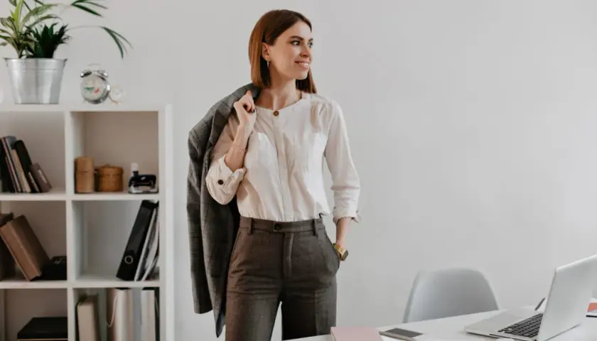 Mujer con un elegante outfit oficina: camisa blanca, pantalón gris y chaqueta a cuadros.